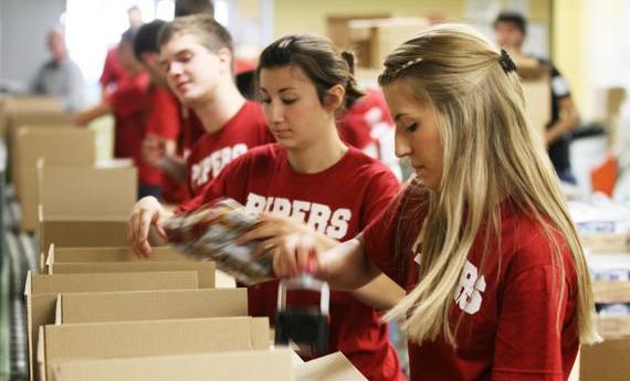 Three 뿪¼ student wearing red "PIPERS" shirts taping cardboard boxes while volunteering