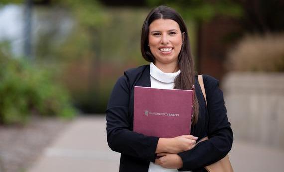 An MBA graduate student from 뿪¼'s School of Business holding a folder and smiling at the camera