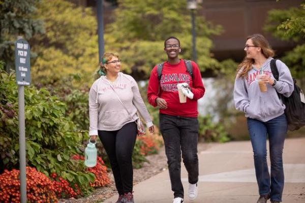 Three 뿪¼ students walking and talking outside on campus in the fall