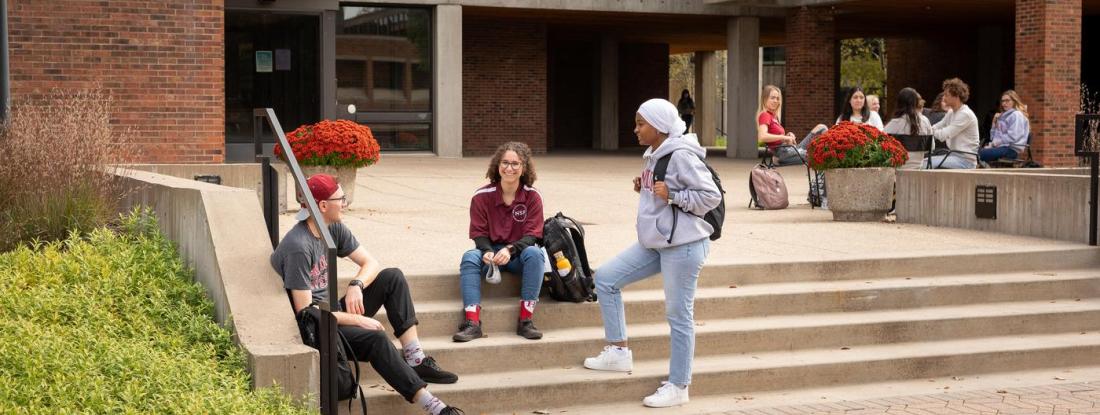 Three 뿪¼ students gathered on a set of outdoor stairs on campus